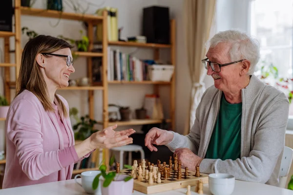 Adult daughter visiting her senior father at home and playing chess together. — Foto Stock