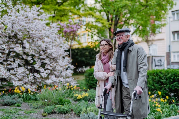 Idős férfi gyalogos keret és felnőtt lánya a szabadban egy séta a parkban. — Stock Fotó