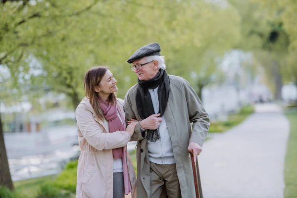 Happy senior man with walking stick and adult daughter outdoors on a walk in park. — Fotografia de Stock