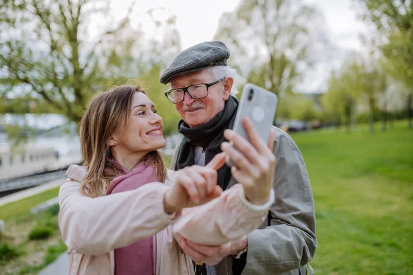 Happy senior man and his adult daughter taking selfie outdoors on a walk in park. — Fotografia de Stock