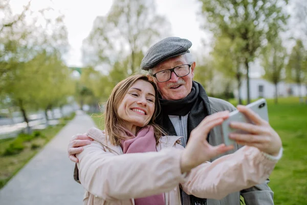 Happy senior man and his adult daughter taking selfie outdoors on a walk in park. — Stock Fotó