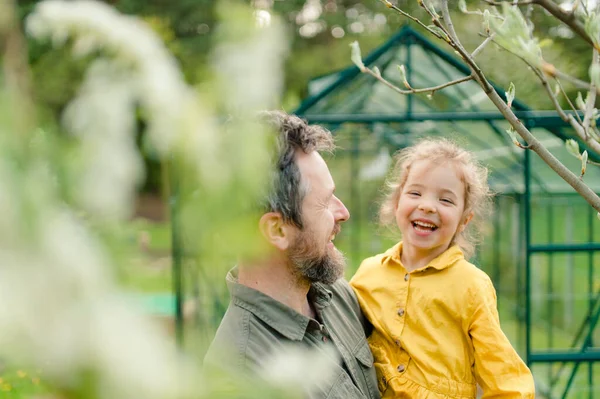 Father with his little daughter laughing in front of eco greenhouse, sustainable lifestyle. — Foto de Stock