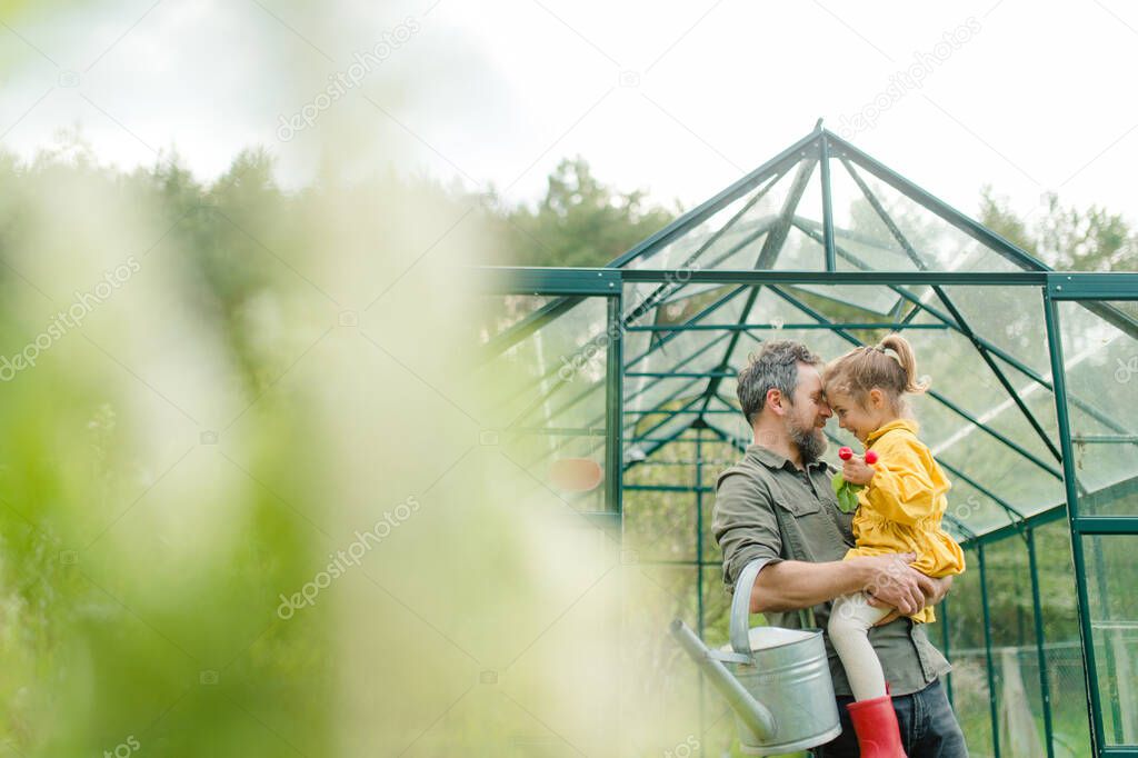 Father with his little daughter bonding in front of eco greenhouse, sustainable lifestyle.