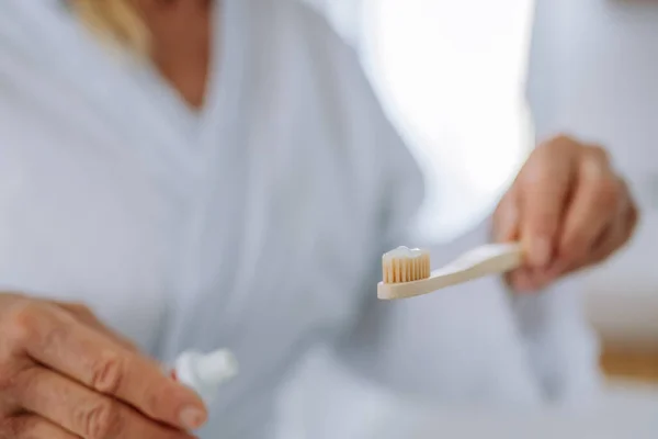 Gros plan de la femme tenant une brosse à dents en bois et du dentifrice naturel dans la salle de bain, mode de vie durable. — Photo