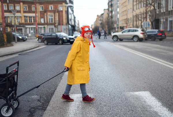 Kleines Mädchen mit Down-Syndrom überquert Straße und zieht Wagen. — Stockfoto