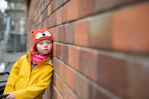 Kleines Mädchen mit Down-Syndrom lehnt im Winter an Ziegelwand. — Stockfoto