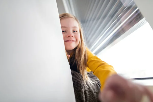 Glückliches kleines Mädchen mit Down-Syndrom sitzt zu Hause am Fenster. — Stockfoto