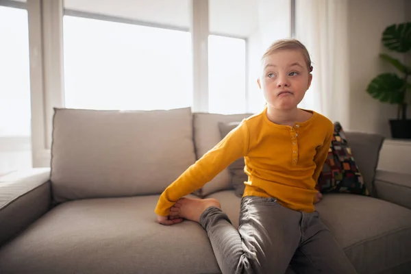 Trauriges kleines Mädchen mit Down-Syndrom sitzt zu Hause auf Sofa. — Stockfoto