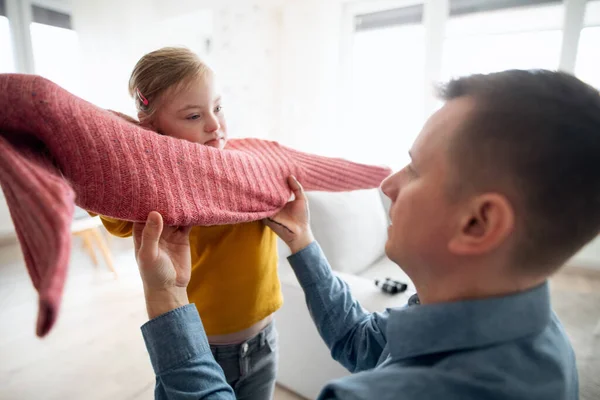Otec pomáhá své malé dceři s Downovým syndromem nosit svetr doma. — Stock fotografie