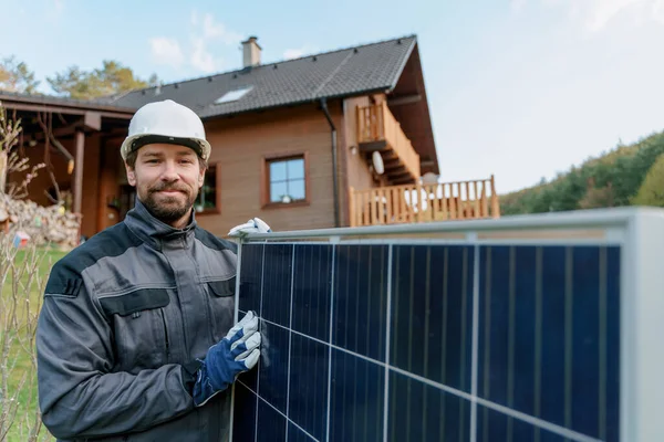 Uśmiechnięty złota rączka instalator słoneczny niosący moduł słoneczny podczas instalacji systemu paneli słonecznych w domu. — Zdjęcie stockowe