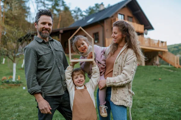 Ευτυχισμένη οικογένεια στέκεται κοντά στο σύγχρονο σπίτι τους, χαμογελούν και βλέπουν τα φωτογραφικών μηχανών — Φωτογραφία Αρχείου
