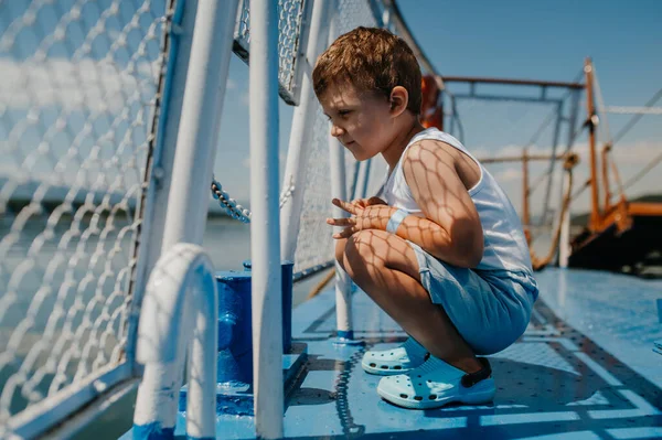 Kleine nieuwsgierige jongen kijkt naar het water van de motorboot. — Stockfoto