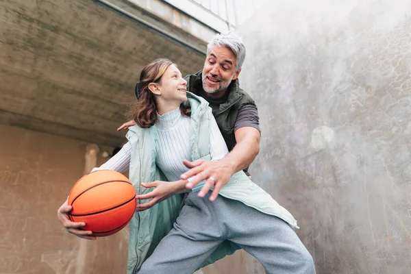 Gelukkig vader en tienerdochter basketballen buiten aan het hof. — Stockfoto