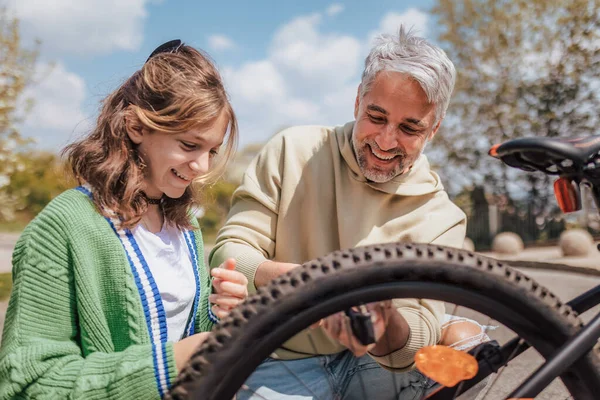 Glücklicher Vater mit Teenager-Tochter repariert Fahrrad auf Straße in der Stadt. — Stockfoto