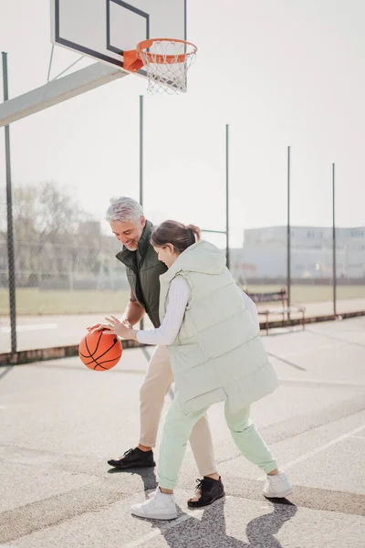 Happy father and teenage daughter playing basketball outside at court. — ストック写真