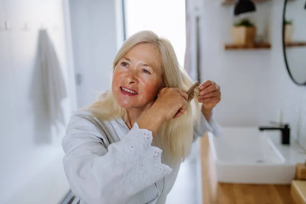 在浴室里用木制梳子梳理头发的漂亮老妇人，可持续的生活方式. — 图库照片