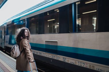 Tren istasyonunda, bavullu, mutlu genç bir gezgin kadın tren istasyonunda bekliyor.