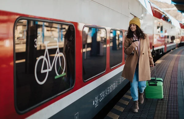 駅のホームで電車の中で荷物とコーヒーボードのカップを持つ幸せな若い旅行者の女性 — ストック写真