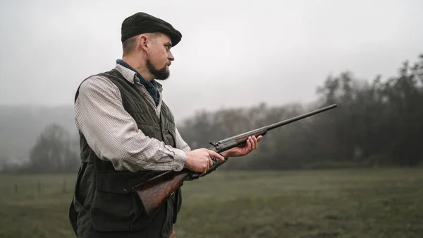 Hombre cazador en ropa de tiro tradicional en el campo apuntando con escopeta. —  Fotos de Stock