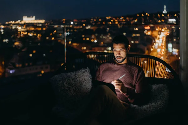 Młody Afroamerykanin Siedzący Balkonie Widokiem Miasto Korzystający Tabletu Nocy — Zdjęcie stockowe
