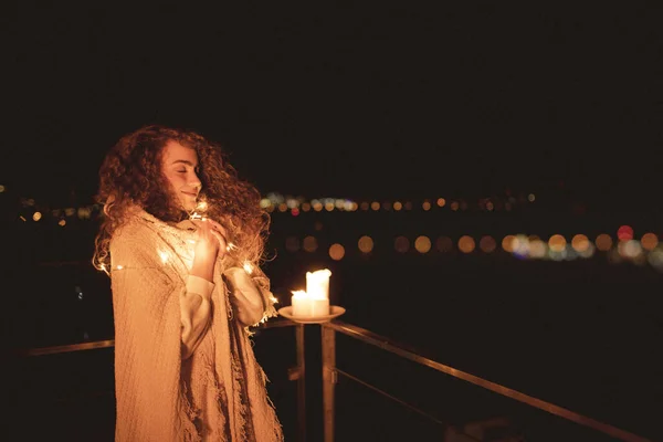 一位穿着毛毯 从容的年轻女子站在阳台上 夜晚点着蜡烛 享受着奢华的生活 — 图库照片