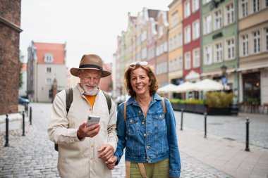 Mutlu yaşlı turistlerin portresi gülümseyen, el ele tutuşan, tarihi şehirde akıllı telefon kullanan