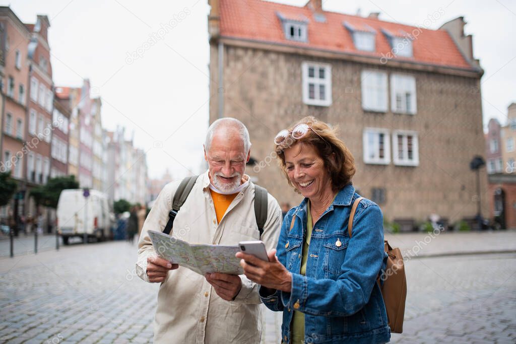 A portrait of happy senior couple tourists using map outdoors in town street