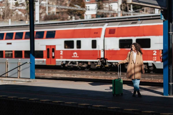 駅のホームで電車を待っている荷物を持つ若い旅行者の女性 バックグラウンドでの列車 — ストック写真