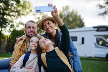 A happy young family with two children taking selfie with caravan at background outdoors. clipart