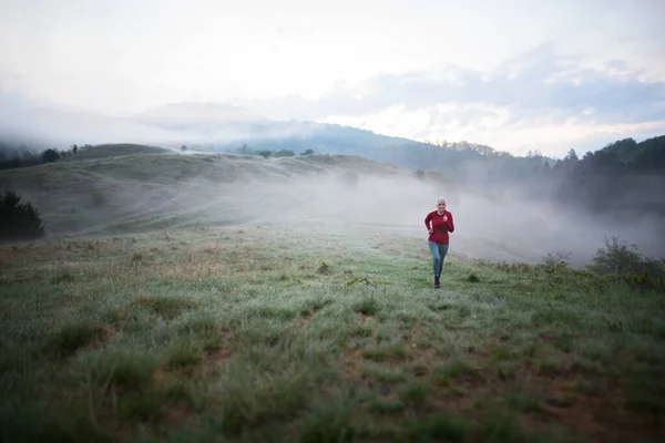 Starsza Kobieta Jogging Przyrodzie Wczesnym Rankiem Mgłą Górami Tle — Zdjęcie stockowe