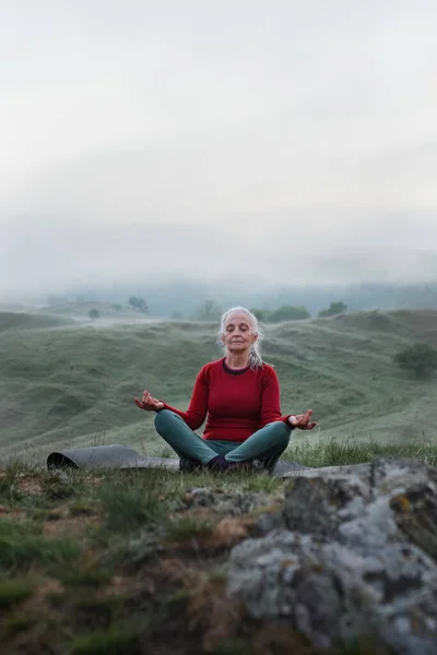 Starsza Kobieta Ćwiczy Oddychanie Naturze Wczesnym Rankiem Mgłą Górami Tle — Zdjęcie stockowe