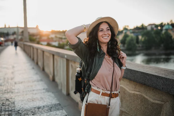 一个年轻美丽的女旅行家背着背包在阳光明媚的城市里走过桥 — 图库照片