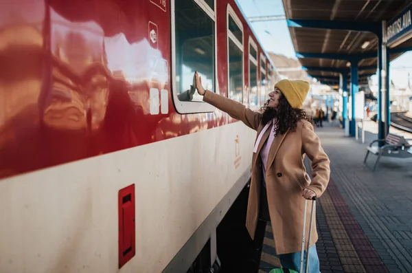 電車の中で誰かを振って プラットフォームに立って別れを告げる荷物を持つ若い旅行者の女性 — ストック写真