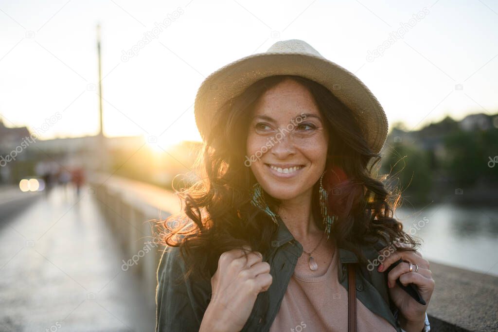 A young beautiful female traveler with backpack walking through bridge on sunny day in city.