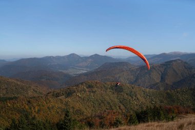 Arka planda dağ ile mavi gökyüzünde uçan bir paraglider..