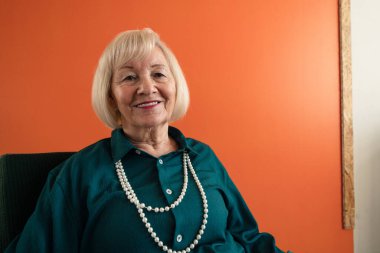 Gülümseyen, zarif, yaşlı bir kadın koltukta oturuyor.