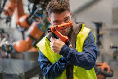 Down sendromlu genç bir adam endüstriyel fabrikada çalışırken planlara bakıyor, sosyal bütünleşme kavramı..