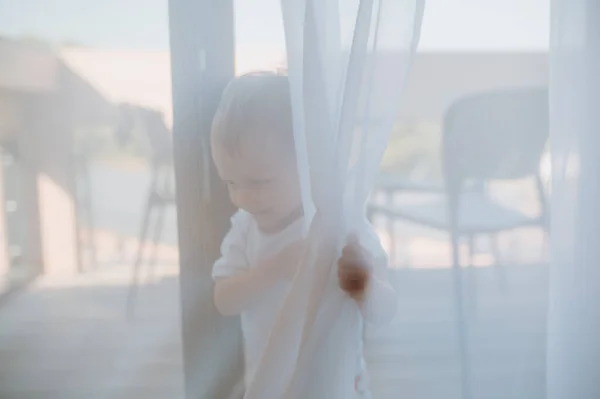 一个可爱的小女孩在家里躲在窗帘后面玩耍 — 图库照片