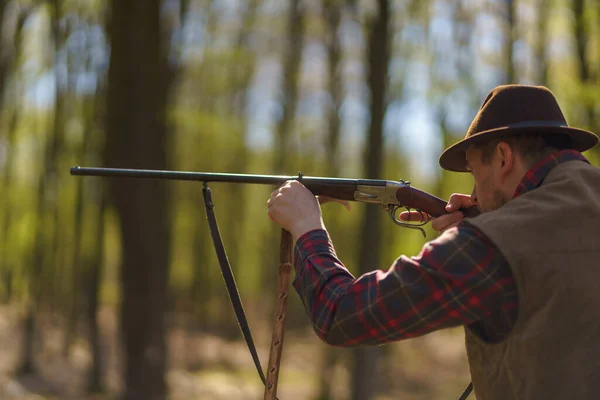 A hunter man aiming with rifle gun on prey in forest.