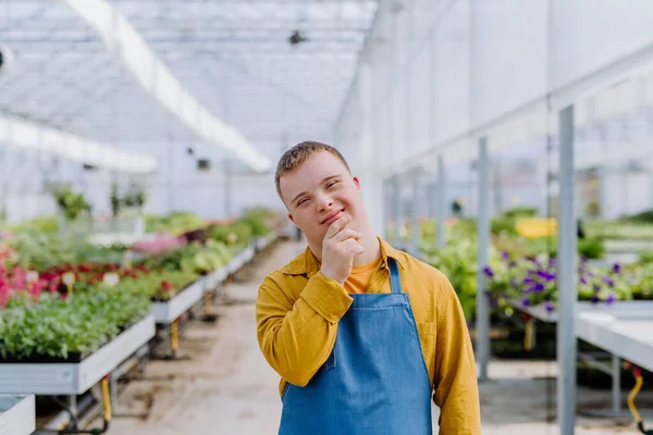 A young employee with Down syndrome working in garden centre, looking at camera.