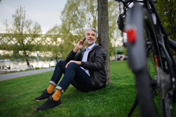 公園の芝生に自転車で座っているビジネスマン スマートフォンを使用しています 代替輸送の概念 — ストック写真