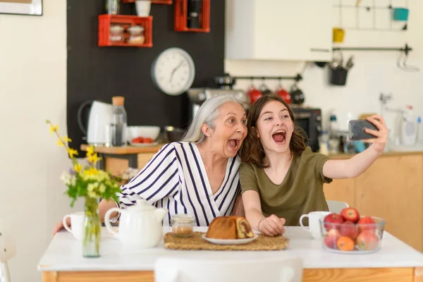 Szczęśliwa Starsza Babcia Nastoletnim Dziadkiem Siedzącym Kuchni Robiącym Selfie Smartfonem — Zdjęcie stockowe