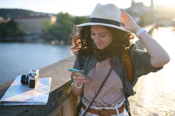 在阳光普照的城市 一位年轻美丽的女旅行者站在桥上 用手机描绘着她的模样 — 图库照片