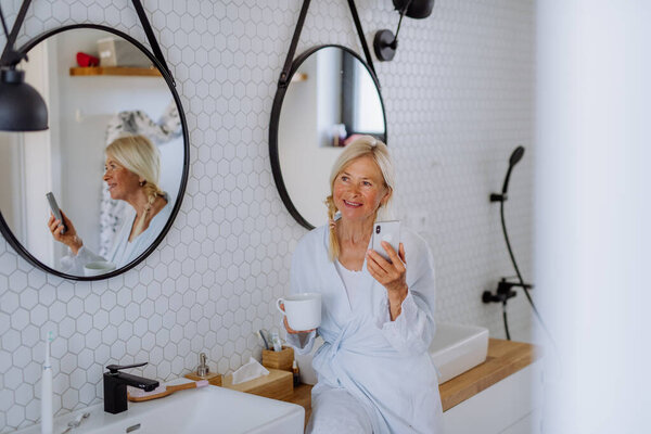 Beautiful Senior Woman Bathrobe Drinking Tea Using Smartphone Bathroom Relax Royalty Free Stock Photos