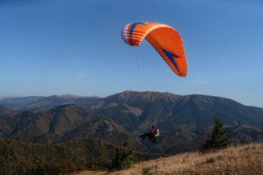 Mavi gökyüzünde uçan paragliderler ve arka planda dağ.