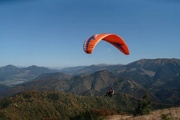 Arka planda dağ ile mavi gökyüzünde uçan bir paraglider..