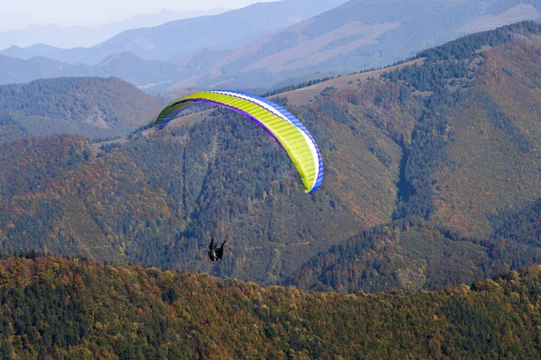Mavi gökyüzünde uçan paragliderler ve arka planda dağ.