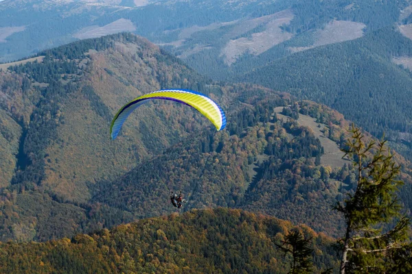 Arka planda dağ ile mavi gökyüzünde uçan bir paraglider..