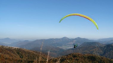 Mavi gökyüzünde uçan paragliderler ve arka planda dağ.