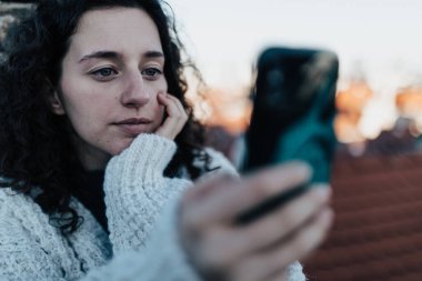 Mutsuz genç bir kadın dinleniyor ve çatıda oturuyor şehir manzaralı ve selfie çekiyor..
